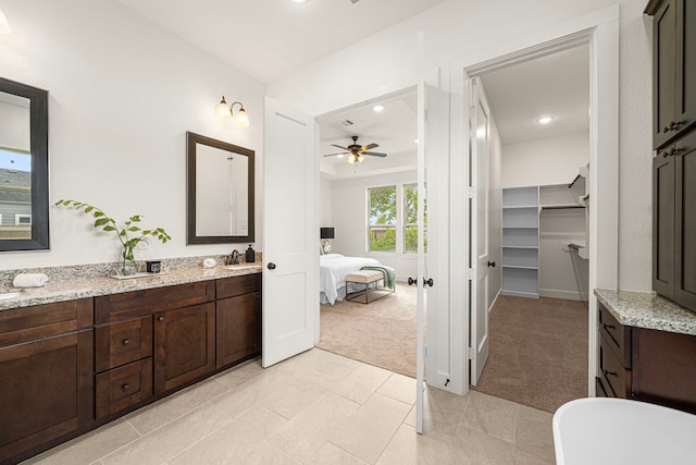 ensuite bathroom featuring connected bathroom, ceiling fan, vanity, a spacious closet, and a soaking tub