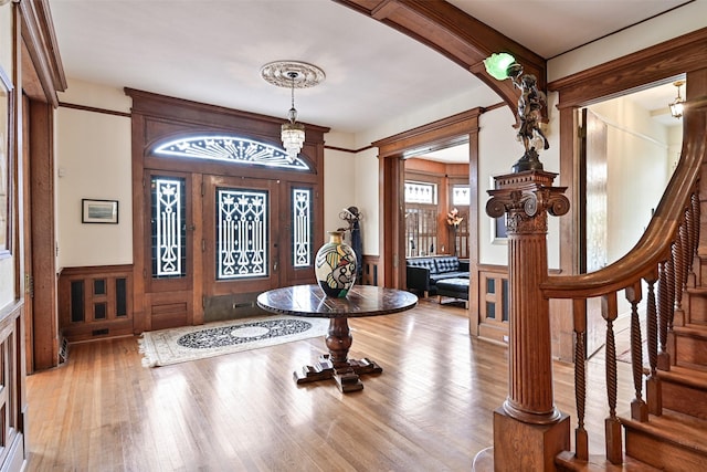 foyer entrance featuring arched walkways, wood finished floors, a wainscoted wall, a decorative wall, and stairs