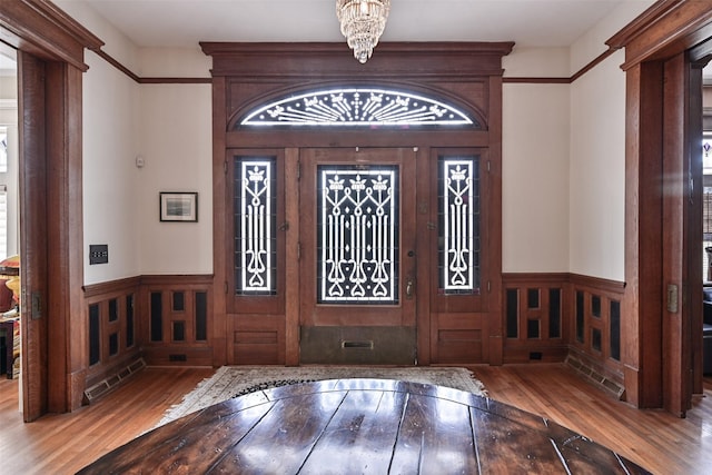 entrance foyer with wood-type flooring, wainscoting, ornate columns, and a chandelier