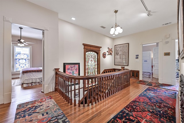 corridor featuring an upstairs landing, wood finished floors, visible vents, and an inviting chandelier