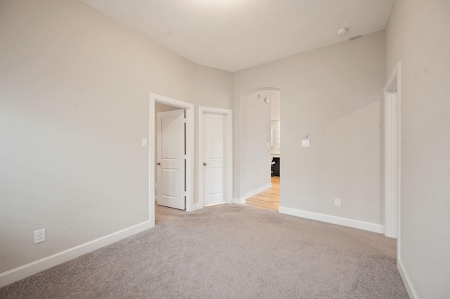 carpeted empty room featuring baseboards and arched walkways