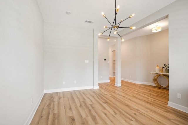 empty room with arched walkways, visible vents, light wood-type flooring, and a chandelier
