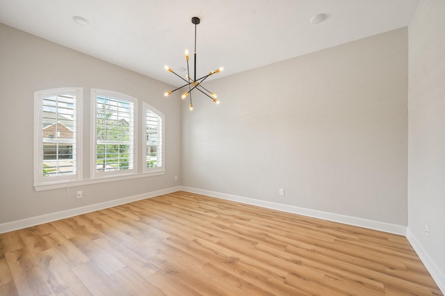 empty room featuring baseboards, light wood-type flooring, and a notable chandelier