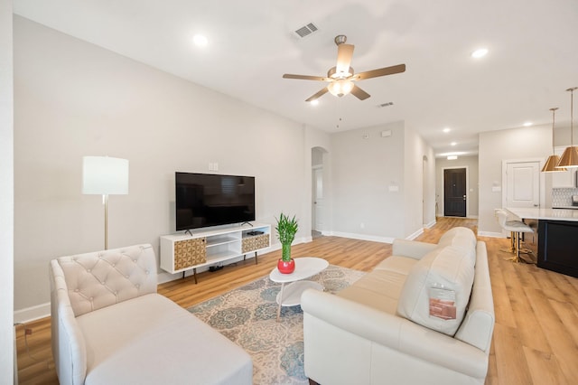 living area featuring visible vents, arched walkways, light wood-style flooring, and ceiling fan