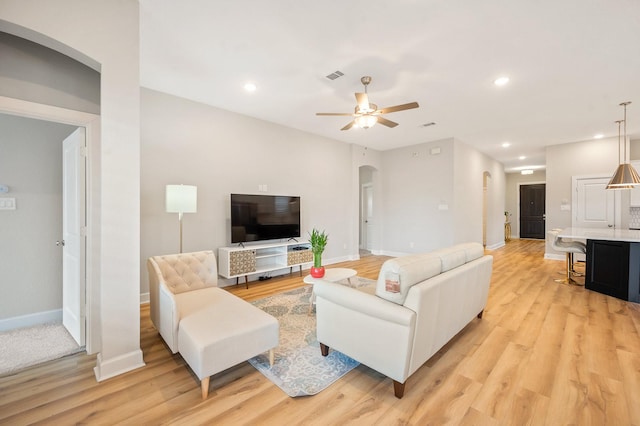 living area featuring baseboards, arched walkways, light wood finished floors, and ceiling fan