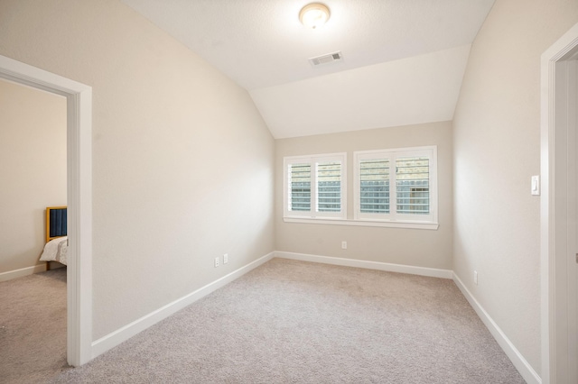 unfurnished room featuring baseboards, light carpet, lofted ceiling, and visible vents