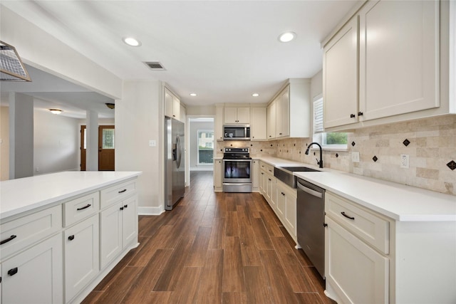 kitchen with appliances with stainless steel finishes, a sink, backsplash, visible vents, and dark wood-style floors
