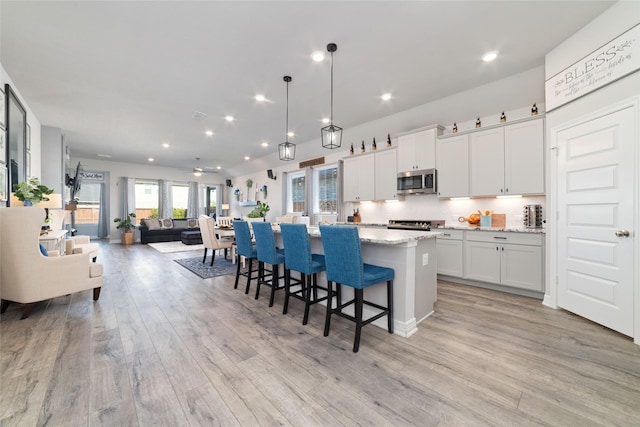 3040 Cirrus Heights Ct, Katy, TX 77493 - kitchen featuring stainless steel microwave, light wood finished floors, open floor plan, a center island, and white cabinets