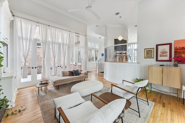 living area with a ceiling fan, a towering ceiling, crown molding, visible vents, and light wood finished floors