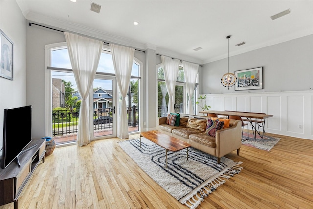 living area with visible vents, crown molding, a notable chandelier, a decorative wall, and light wood-style flooring