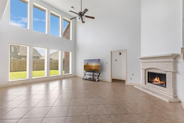 unfurnished living room with light tile patterned flooring, a fireplace, a ceiling fan, baseboards, and a towering ceiling