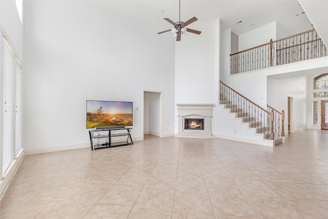 unfurnished living room featuring ceiling fan, a lit fireplace, tile patterned floors, and a towering ceiling