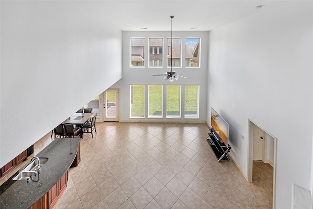 living room with a ceiling fan, plenty of natural light, light tile patterned floors, and a towering ceiling