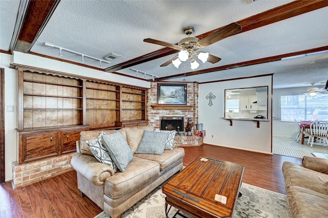 living area featuring a brick fireplace, a ceiling fan, a textured ceiling, and wood finished floors