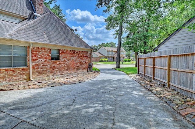 view of side of property with roof with shingles, fence, a chimney, and brick siding