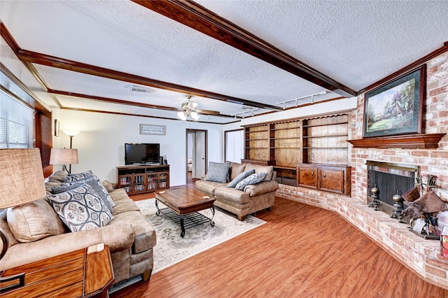 living area with a ceiling fan, a textured ceiling, visible vents, wood finished floors, and beamed ceiling