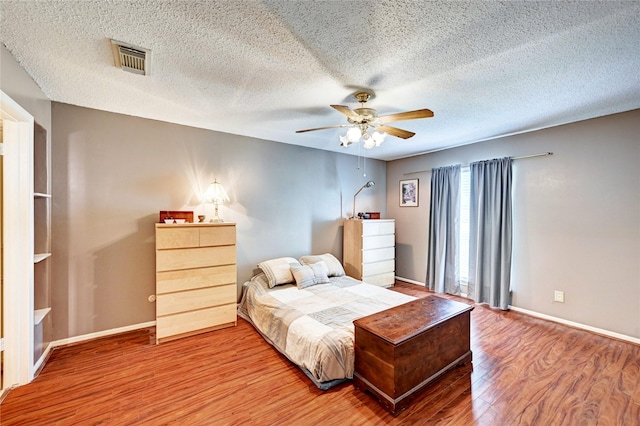 bedroom with baseboards, a textured ceiling, visible vents, and wood finished floors
