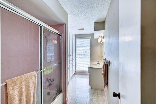 bathroom featuring bath / shower combo with glass door, vanity, a textured ceiling, and visible vents
