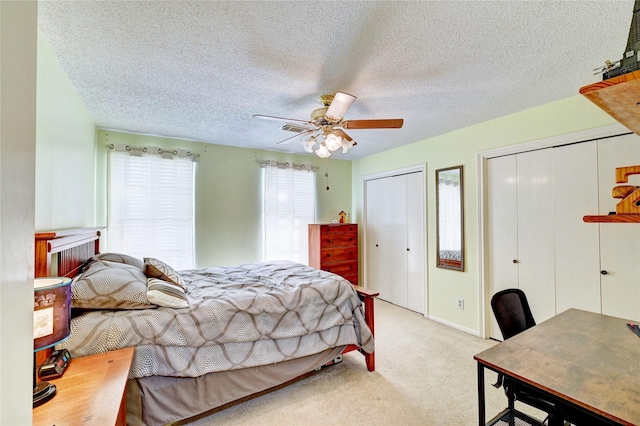 carpeted bedroom featuring two closets, a textured ceiling, visible vents, and ceiling fan