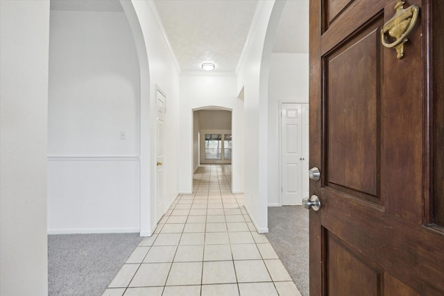 foyer featuring crown molding, light carpet, baseboards, arched walkways, and light tile patterned floors