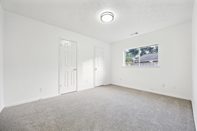 carpeted empty room with a textured ceiling, baseboards, and visible vents