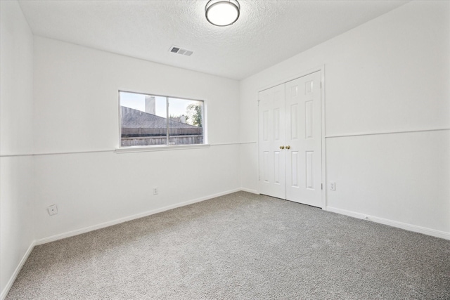 empty room featuring carpet flooring, a textured ceiling, visible vents, and baseboards