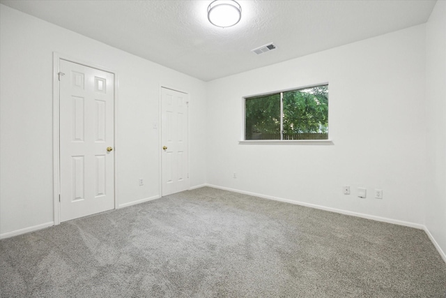 unfurnished room featuring a textured ceiling, baseboards, visible vents, and carpet