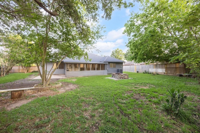 rear view of house featuring a lawn, fence private yard, a sunroom, and an outdoor fire pit