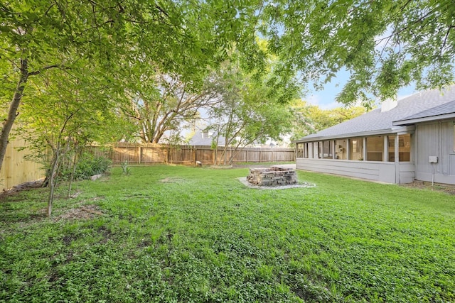 view of yard with a fenced backyard, a sunroom, and an outdoor fire pit