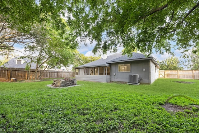 back of house with central AC, a sunroom, a fenced backyard, a lawn, and a fire pit