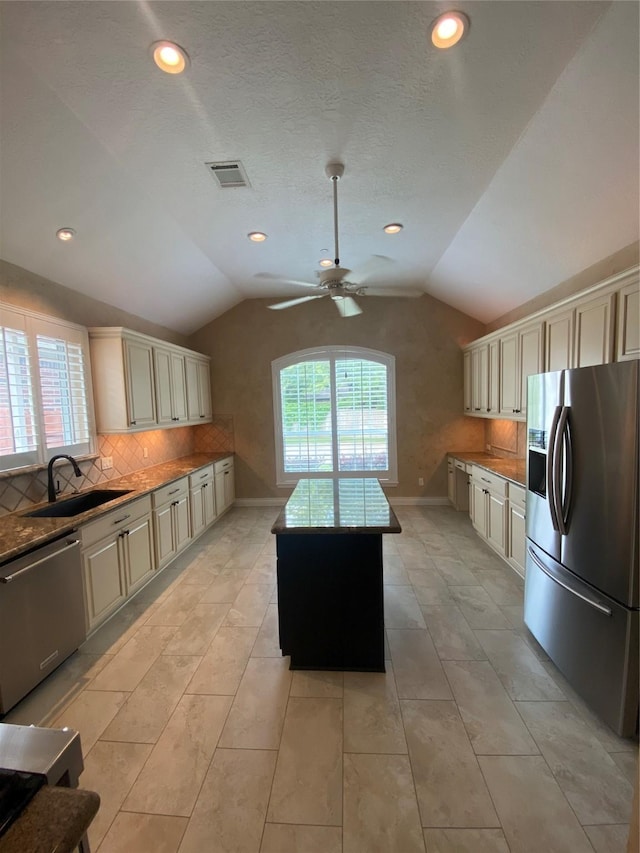 kitchen with cream cabinetry, appliances with stainless steel finishes, a sink, and lofted ceiling