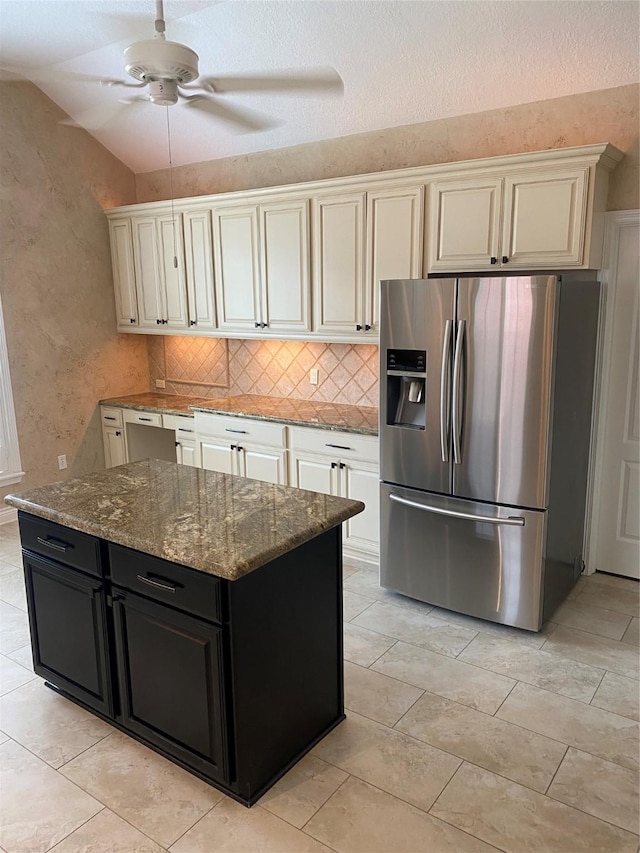 kitchen with decorative backsplash, dark cabinets, stone counters, vaulted ceiling, and stainless steel fridge