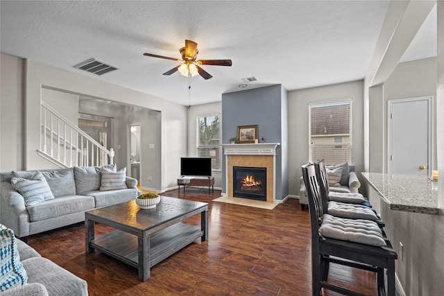 living room with a ceiling fan, visible vents, a fireplace, wood finished floors, and stairs