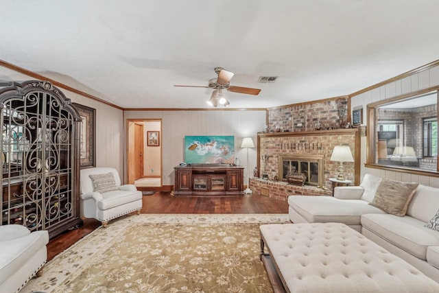 living room with ceiling fan, visible vents, crown molding, a fireplace, and wood finished floors