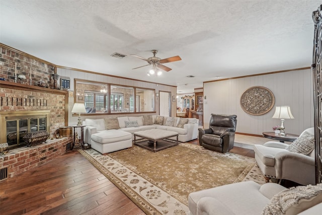 living room featuring crown molding, visible vents, a brick fireplace, hardwood / wood-style floors, and ceiling fan