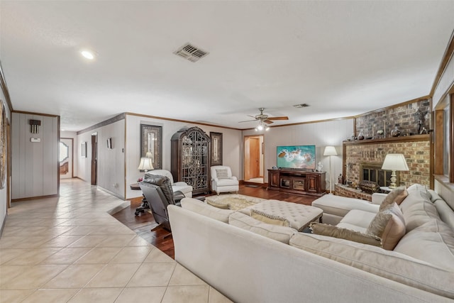 living room featuring a ceiling fan, visible vents, crown molding, a fireplace, and light tile patterned floors