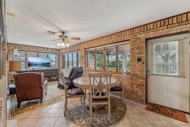 dining room with visible vents, brick wall, a textured ceiling, a ceiling fan, and light tile patterned floors