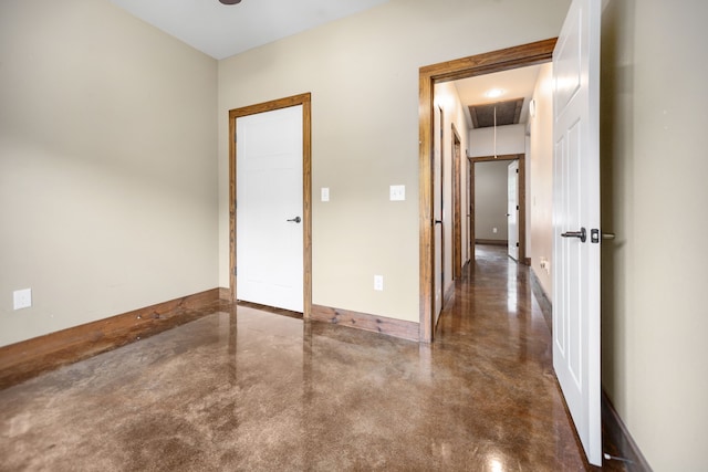 unfurnished room with finished concrete floors, attic access, and baseboards