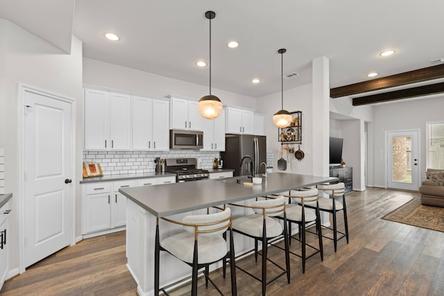 kitchen featuring dark wood-style flooring, beamed ceiling, a breakfast bar area, appliances with stainless steel finishes, and backsplash