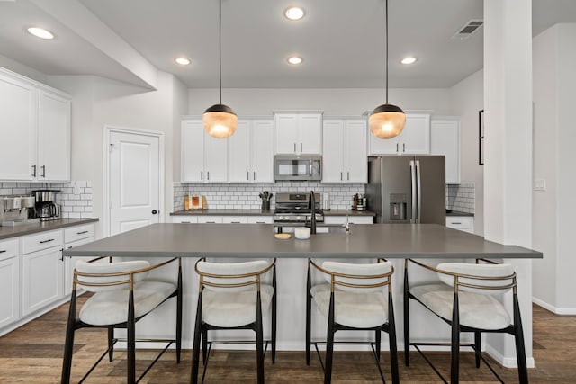 kitchen featuring a kitchen island with sink, dark countertops, a sink, backsplash, and stainless steel appliances