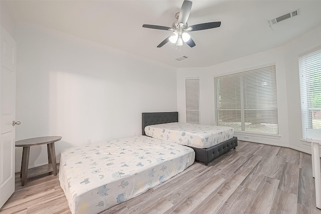 bedroom featuring crown molding, a ceiling fan, wood finished floors, and visible vents