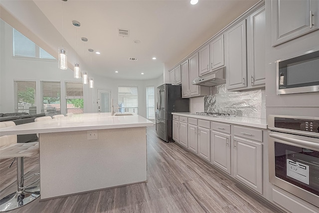 kitchen with visible vents, open floor plan, under cabinet range hood, a sink, and stainless steel appliances