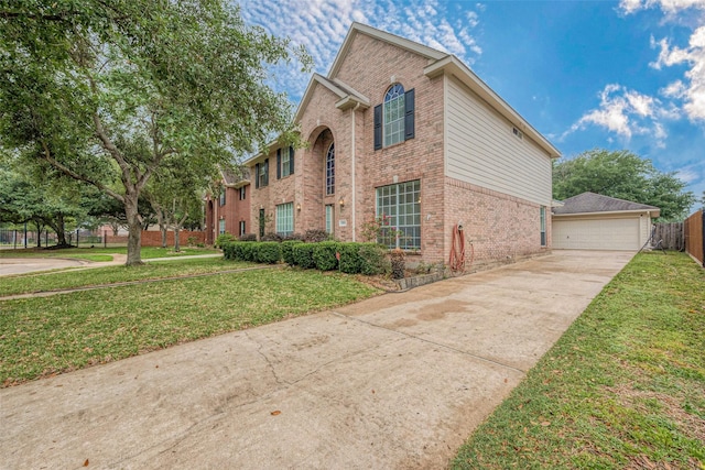 view of front of property featuring a detached garage, brick siding, fence, and a front yard