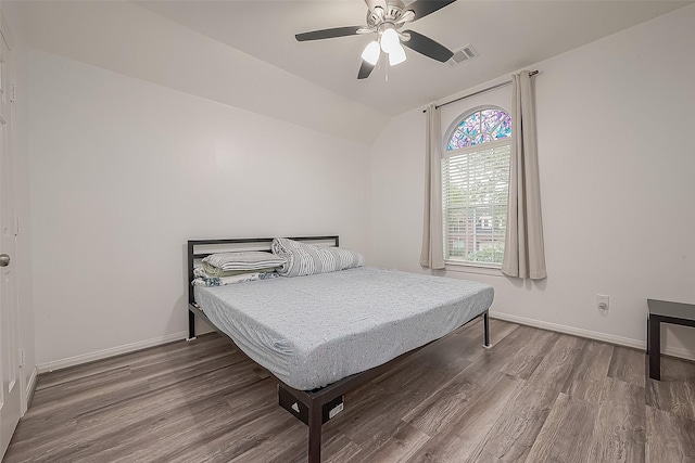 bedroom featuring baseboards, visible vents, wood finished floors, and lofted ceiling