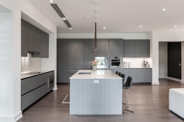 kitchen with modern cabinets, a center island with sink, light countertops, a sink, and gray cabinetry