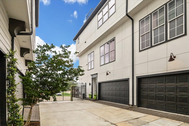 view of side of home featuring an attached garage, driveway, and a gate