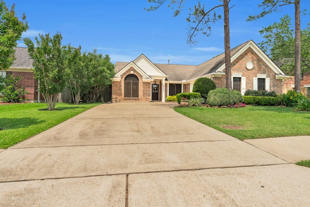 ranch-style home with concrete driveway, brick siding, a shingled roof, and a front lawn