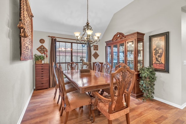 dining space featuring baseboards, a notable chandelier, vaulted ceiling, and light wood-style floors