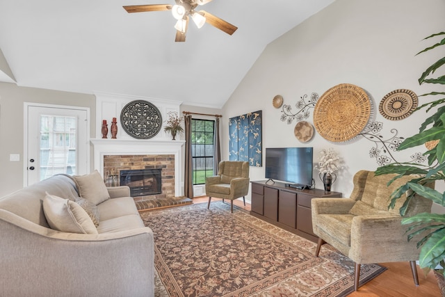 living area featuring high vaulted ceiling, a ceiling fan, wood finished floors, and a brick fireplace