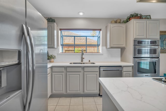 kitchen featuring appliances with stainless steel finishes, light stone counters, a sink, light tile patterned floors, and gray cabinetry